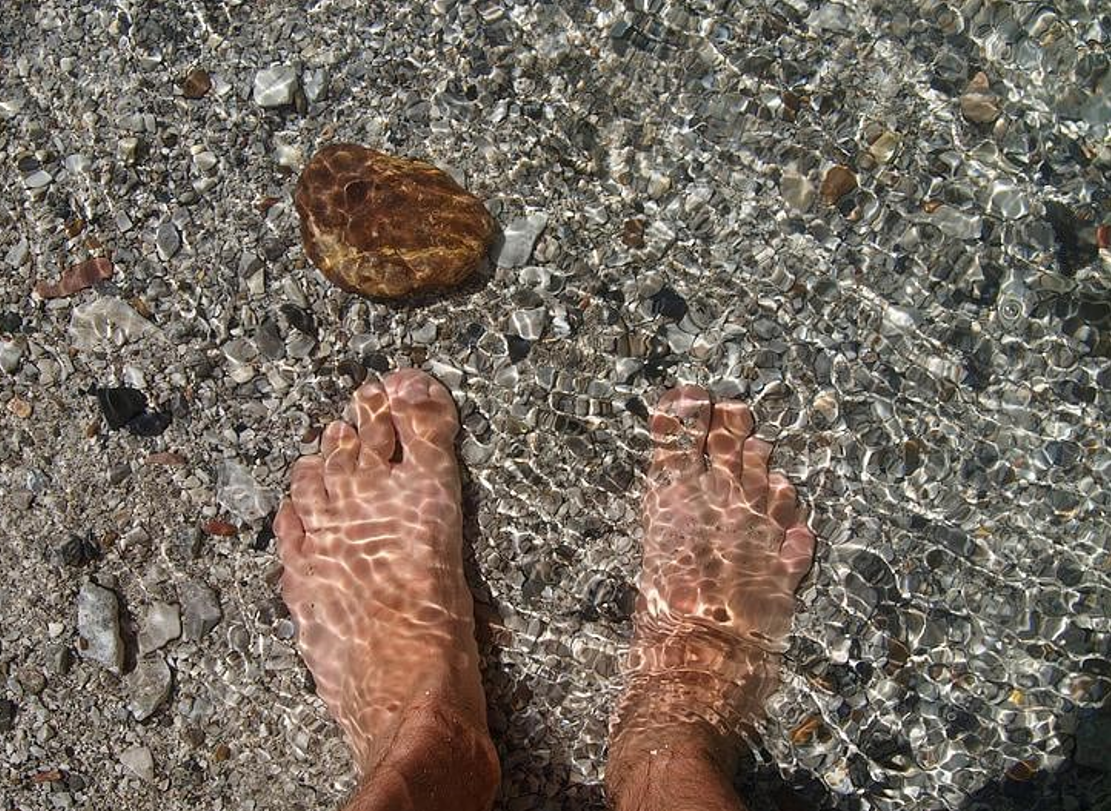 Bare feet resting in clear, shallow water